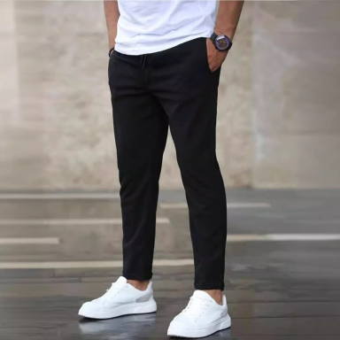 Hombre de pie con pantalones negros y zapatillas blancas, manos en los bolsillos.